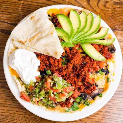 A plate of vibrant Mexican food featuring chorizo, avocado slices, sour cream, and fresh salsa on a tortilla.