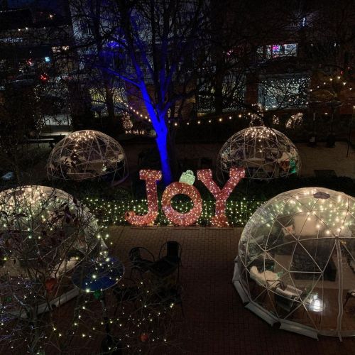A festive outdoor scene with illuminated domes and a large "JOY" sign surrounded by twinkling lights.