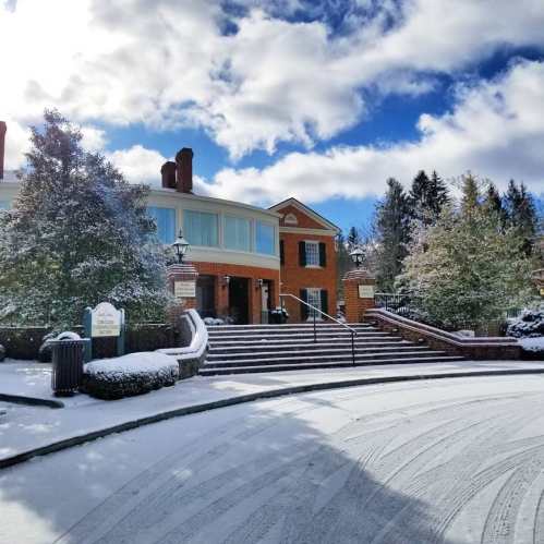 A brick building with snow-covered steps and trees, under a blue sky with fluffy clouds.