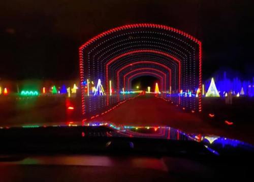 A colorful light display forms an archway over a road, with vibrant decorations lining the sides.