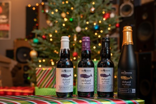 Four bottles of "Richard the Whale" beer in front of a decorated Christmas tree and wrapped gifts.