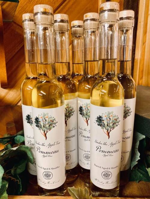 Bottles of Ponmeau apple wine displayed on a wooden shelf, featuring a decorative label with an apple tree design.