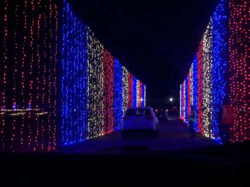 A car drives through a tunnel of colorful lights in red, blue, and white, creating a festive atmosphere at night.
