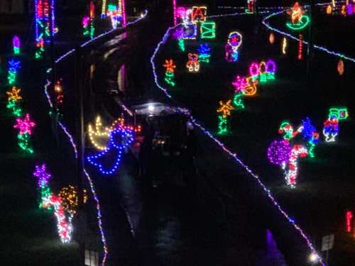 A colorful display of holiday lights illuminates a pathway with various festive decorations and a vehicle in the center.