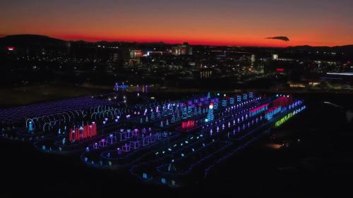 Aerial view of a vibrant light display at dusk, with colorful patterns against a sunset sky.