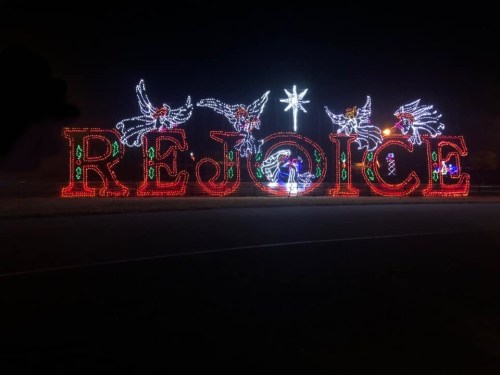 Colorful holiday lights spell "REJOICE" with festive decorations, set against a dark night sky.