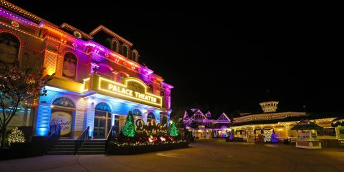Colorful lights illuminate the Palace Theater and surrounding buildings at night, creating a festive atmosphere.