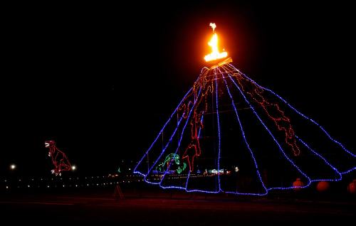 A brightly lit volcano with flames on top, surrounded by colorful holiday lights in a dark night setting.