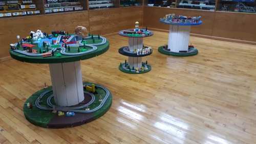 Three circular display tables with toy train sets and miniature landscapes in a wooden room with a polished floor.
