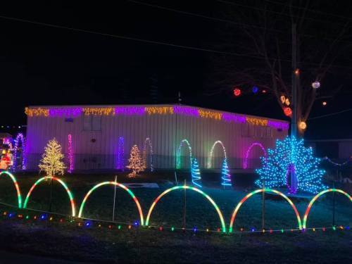 A brightly lit building decorated with colorful Christmas lights, featuring illuminated trees and arches in the yard.