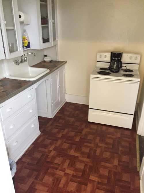 A small kitchen featuring a white stove, coffee maker, sink, and cabinets with a patterned floor.