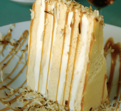 A slice of layered cake drizzled with caramel and sprinkled with coconut flakes on a white plate.