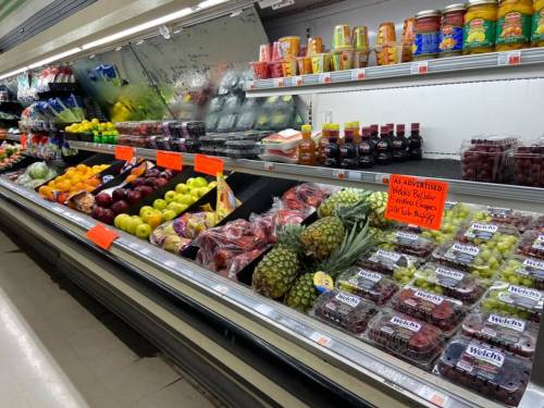 A grocery store produce section with various fruits, vegetables, and jars, featuring colorful signage and organized displays.