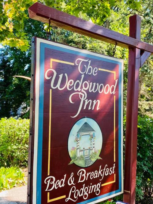 Sign for The Wedgwood Inn Bed & Breakfast, featuring a decorative design and surrounded by greenery.