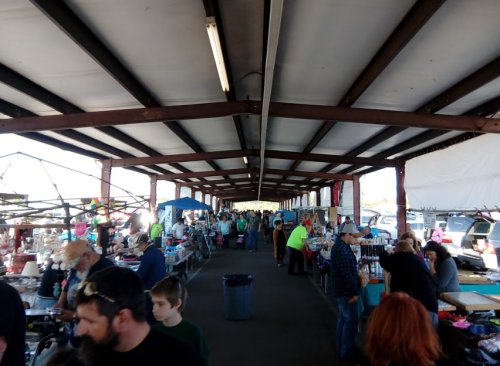 A bustling indoor market with vendors and shoppers, featuring various stalls and a lively atmosphere.