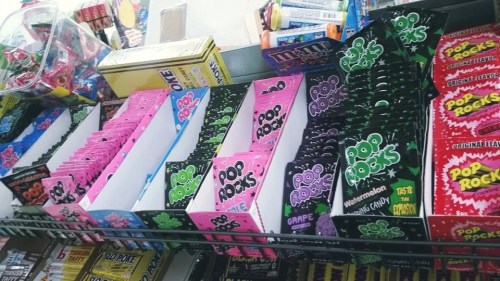 A colorful display of various candy packages, including Pop Rocks in pink and green, arranged on a store shelf.
