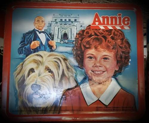 Illustration of a young girl with curly red hair, a dog, and a man in a tuxedo, inspired by the musical "Annie."