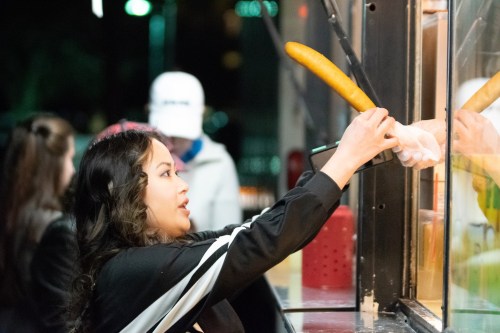 A woman reaches out to receive food from a food truck window at night.