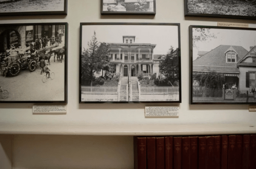 Black and white photo of a historic house, framed and displayed on a wall alongside other vintage images.
