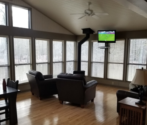 Cozy living area with two chairs, a TV on the wall, and large windows overlooking a wooded view.