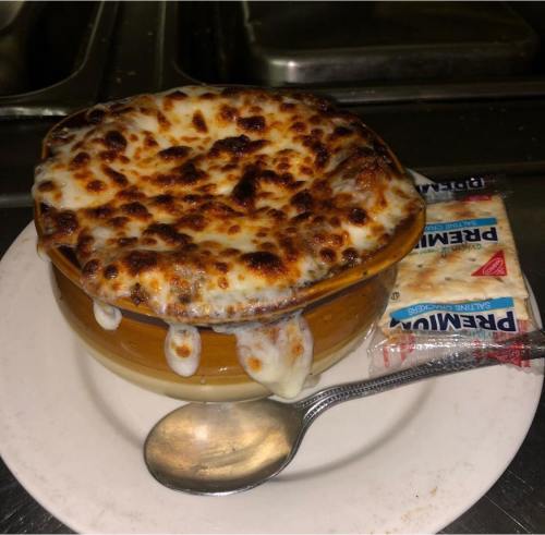 A bowl of cheesy, baked dish with a golden crust, served with a spoon and packets of cream on the side.