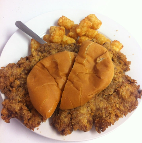 A plate of crispy fried chicken, two split sandwich buns, and a serving of golden tater tots.