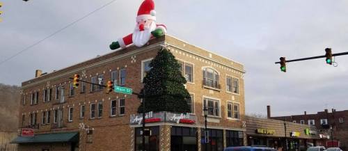 A large inflatable Santa atop a building, with a decorated Christmas tree on the storefront below. Traffic lights visible.