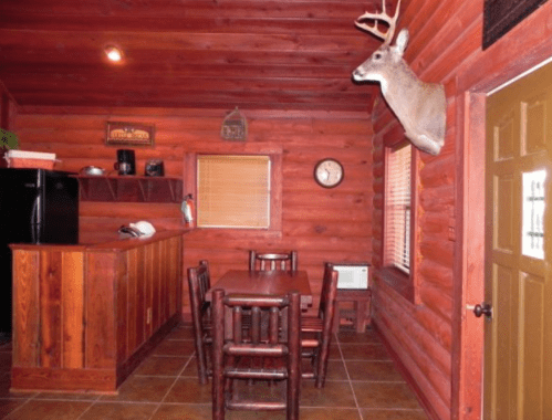 Cozy log cabin interior featuring a dining table, kitchen area, and a mounted deer head on the wall.
