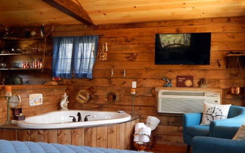 Cozy cabin interior featuring a wooden wall, a jacuzzi tub, a blue chair, and a wall-mounted TV.
