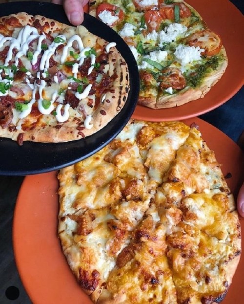 Three pizzas on orange plates: one with white sauce and bacon, one with vegetables and cheese, and a cheesy pizza.