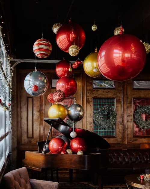 A cozy room with a grand piano, adorned with large red and gold Christmas ornaments hanging from the ceiling.
