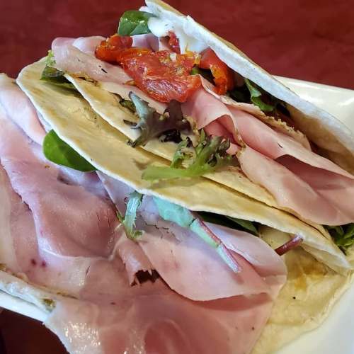 A close-up of a stack of tortillas filled with ham, greens, and sun-dried tomatoes on a plate.