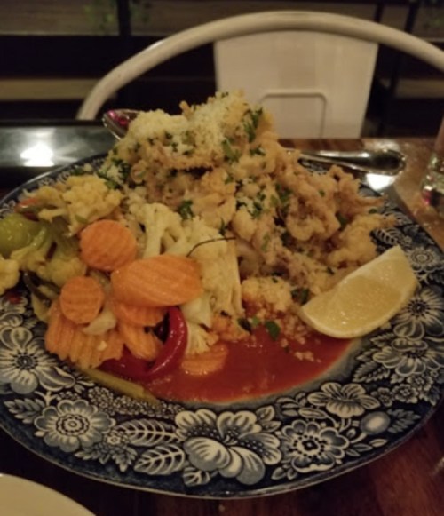 A plate of fried calamari topped with herbs, served with a side of colorful pickled vegetables and a lemon wedge.