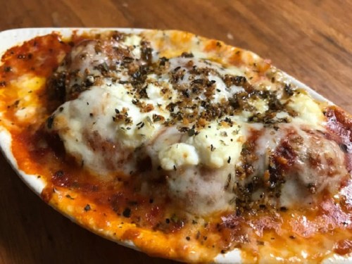Baked dish with meatballs, marinara sauce, melted cheese, and herbs, served in a white oval dish.
