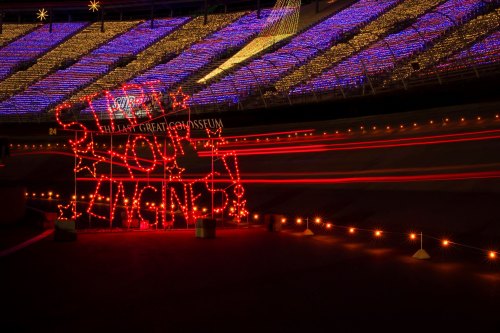 A brightly lit sign reading "Start Your Engine!" in a stadium decorated with colorful lights.