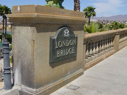 Sign for London Bridge on a stone pillar, with palm trees and a clear sky in the background.