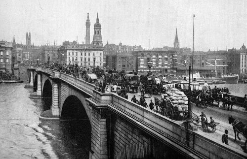 Historic black-and-white photo of a busy bridge with horse-drawn carriages and buildings along the waterfront.