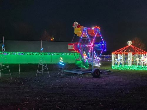 A colorful Ferris wheel and carousel illuminated with festive lights at night, surrounded by glowing decorations.