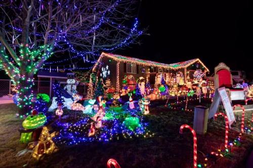 A brightly lit house decorated with colorful Christmas lights and festive lawn ornaments at night.