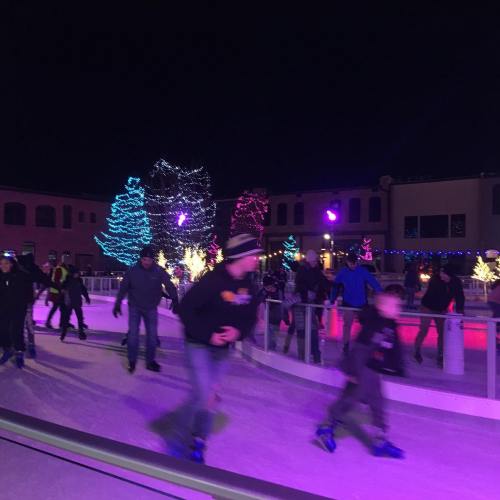 A lively ice skating rink at night, decorated with colorful lights and trees, with people skating and enjoying the atmosphere.