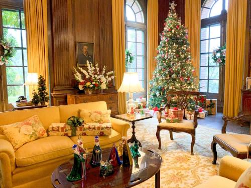 Cozy living room decorated for Christmas, featuring a tree, gifts, and festive decor, with warm lighting and elegant furnishings.