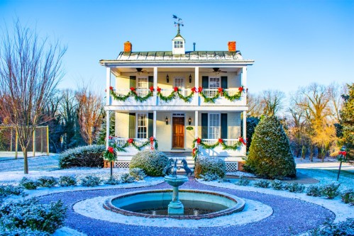 A festive two-story house decorated with holiday garlands, surrounded by snow and a circular fountain in the foreground.