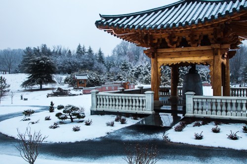 A serene winter scene featuring a traditional gazebo surrounded by snow-covered gardens and trees.
