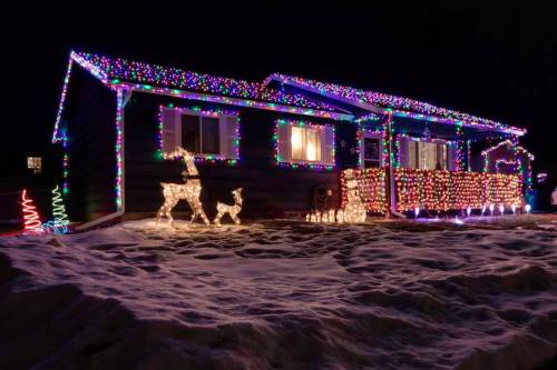 A house decorated with colorful Christmas lights, featuring illuminated reindeer and a snowy yard at night.