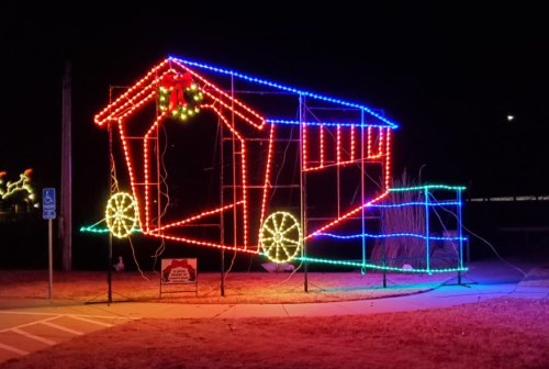 A colorful light display of a covered bridge, illuminated in red, blue, and green against a dark night sky.