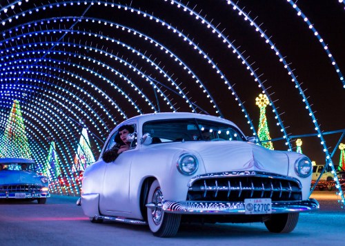 A vintage car drives through a colorful, illuminated tunnel of lights during a festive event at night.