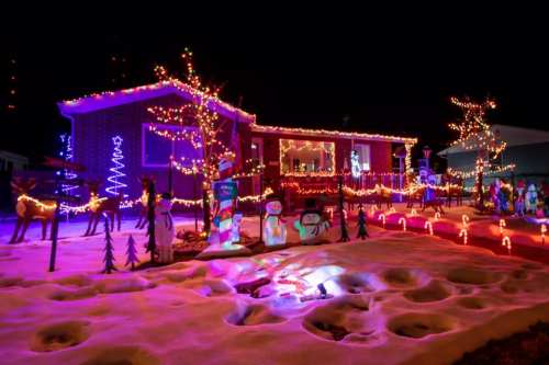 A brightly lit house decorated with colorful Christmas lights and festive figures in a snowy yard at night.