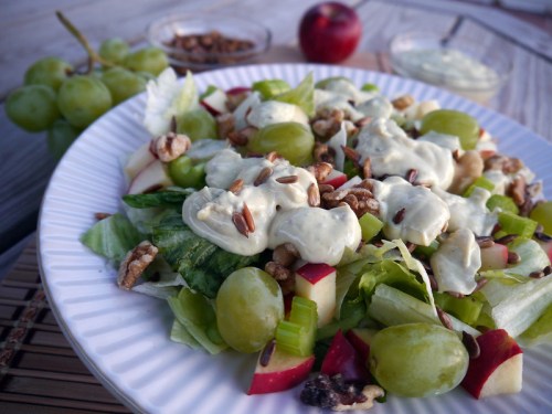 A fresh salad with lettuce, apples, grapes, celery, nuts, and creamy dressing, served on a white plate.