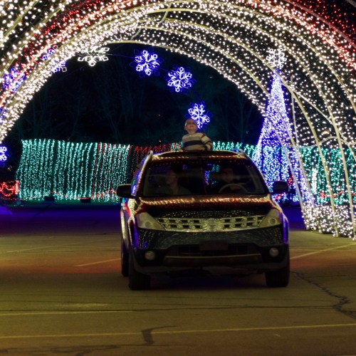 A car drives through a colorful light display with snowflake decorations at night.