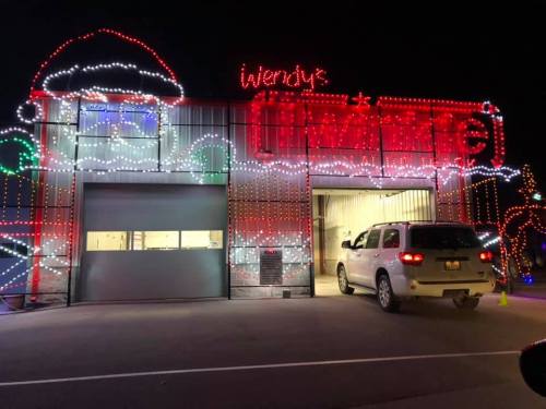 A Wendy's restaurant decorated with colorful holiday lights at night, featuring a festive design and a car in the drive-thru.